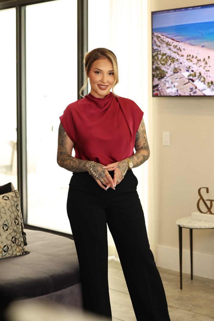 Agata standing in a bright living room, aerial property footage on the screen behind her