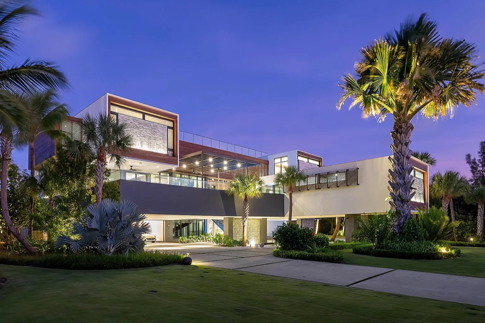 The $15 million beachfront estate at dusk, palms lit against a violet sky