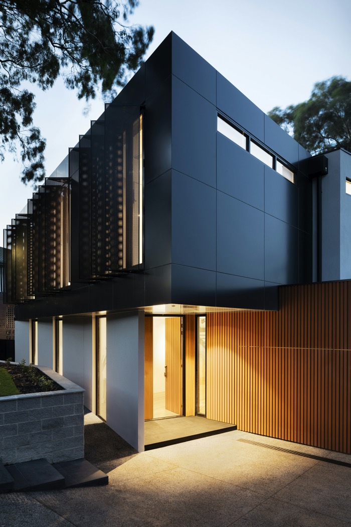 Charcoal residence with cedar cladding and warm entry light at dusk