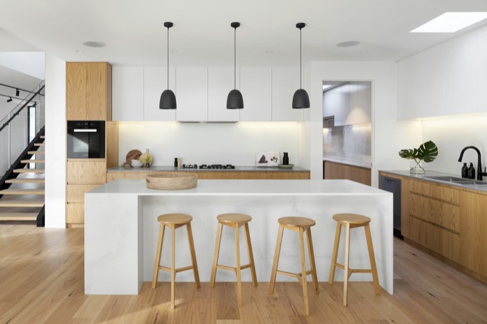 White kitchen with an oak-wrapped island, wooden stools, and black pendant lights