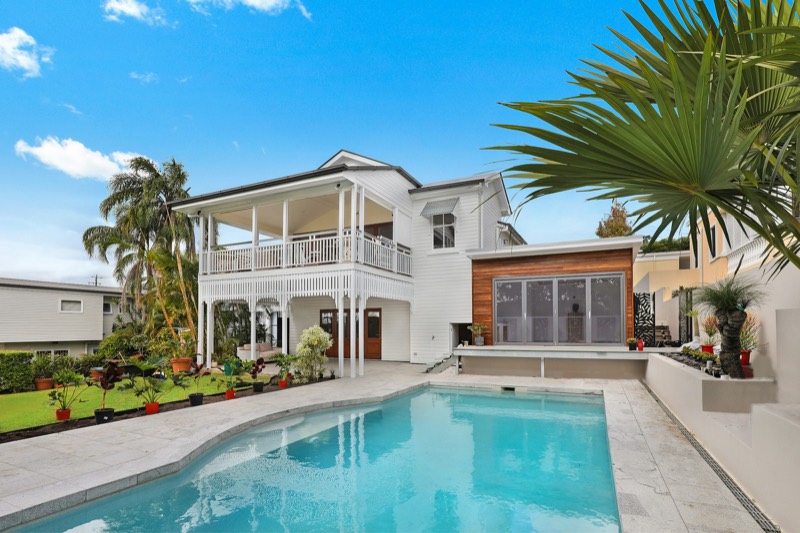 Two-story coastal home with wraparound verandas, palms, and a private pool