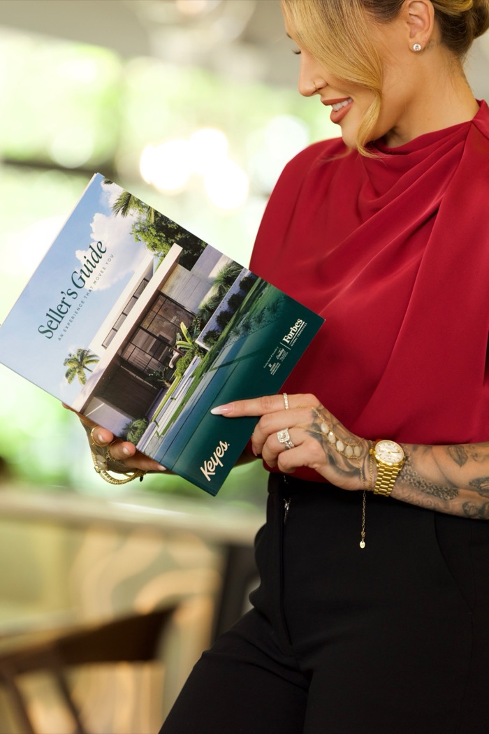Agata smiling over The Keyes Company Seller's Guide, Forbes Global Properties on the cover